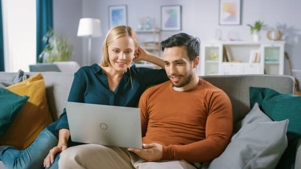istock Happy Lovely Couple Sits on a Sofa at Home, Boyfriend Holds, Browsing through Internet, Doing e-Shopping, Using Streaming Services. Happy Family in Cozy Living Room. 1161176876