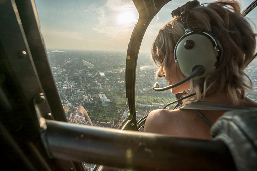 Portrait of beautiful blonde women enjoying helicopter flight. She is amazed by cityscape and wearing pilot headphones.
