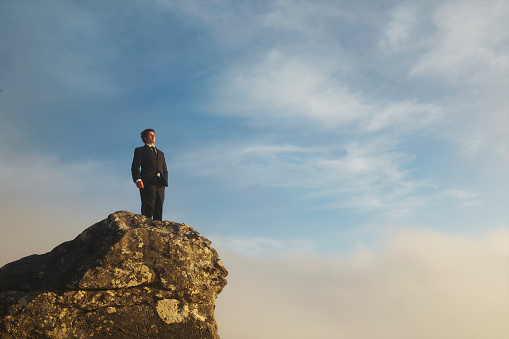 Side Angle low angle view of a businessman at sunset on top of a cliff with dramatic sky and clouds below and above Cape Town South Africa