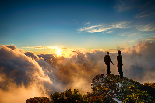 Caucasian Male and Mixed Race Female Businessman and Businesswoman together on top of a mountain at a spectacular sunset shaking hands and looking out Cape Town South Africa