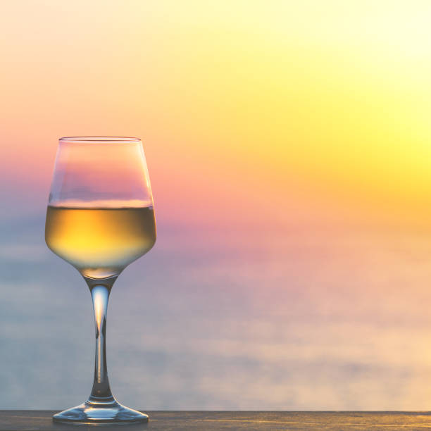 Glass of white wine against sunset. Beautiful summer evening sea view.
