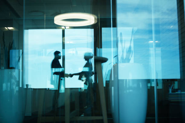We've got ourselves a deal Silhouetted shot of two businesspeople shaking hands in an office mergers and acquisitions photos stock pictures, royalty-free photos & images