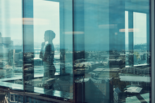 Shot of a businesswoman standing inside a glass building with a reflection of the city in the background