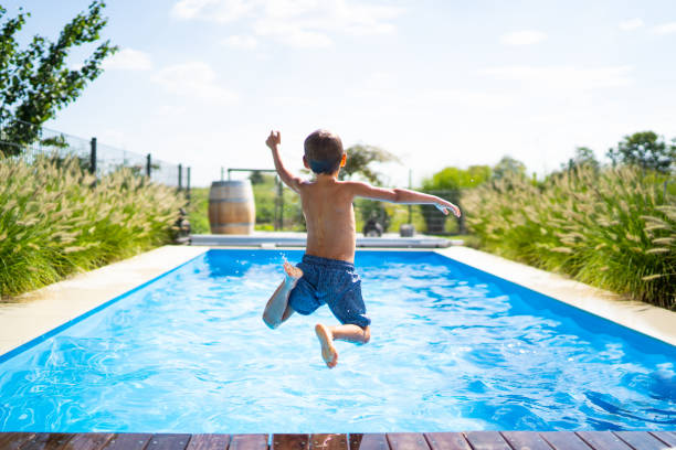hello summer holidays - boy jumping in swimming pool rear view of 4 year old boy jumping into private pool on sunny vacation day - boy is unrecognizable so can be used anonymous summer fun series one boy only photos stock pictures, royalty-free photos & images