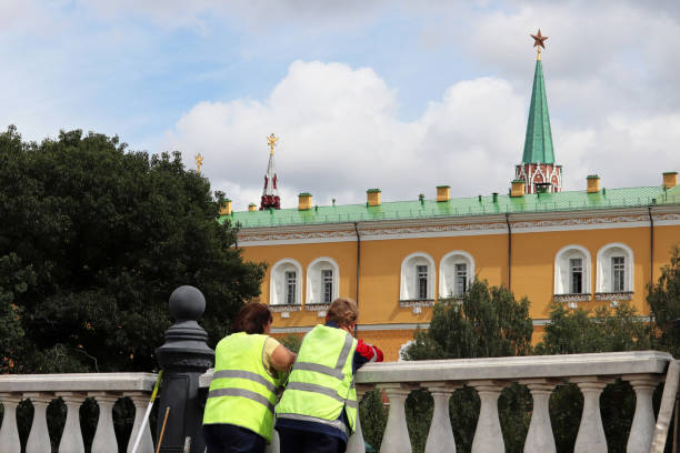 Moscow, Russia - July 2019: Two women in uniform of communal workers tanding on background of Moscow Kremlin in summer. Labour migrants in Russia, concept of street cleaning, garbage removal, low-paid work