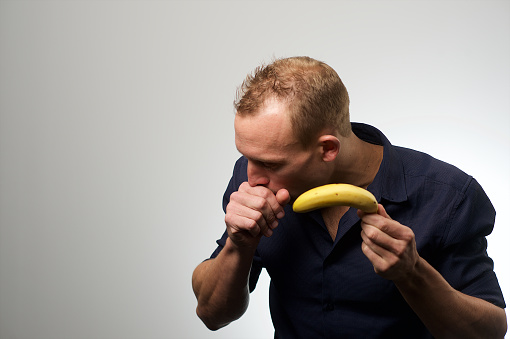 Studio Portrait of a young Caucasian male against a white background and a banana in front of his mouth South Africa