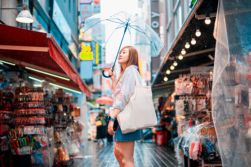spring and raining season activity concept from beauty asian woman travel and shopping with hold her umbrella with city and street food market background