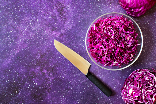 Red cabbage fresh salad in a glass bowl on a dark purple background. Vegetarian healthy food. Top view, copy space
