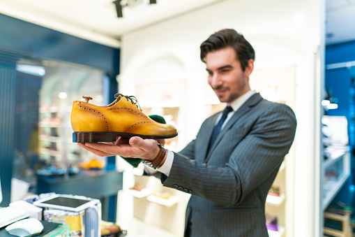 Salesman standing in shopping store and holding modern, elegant yellow shoes in hand, looking at them