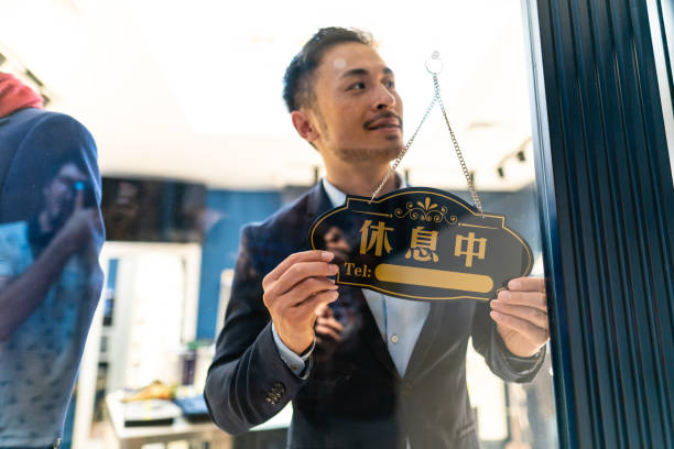 Young Chinese man looking through the window store glass , turning table on open sign
