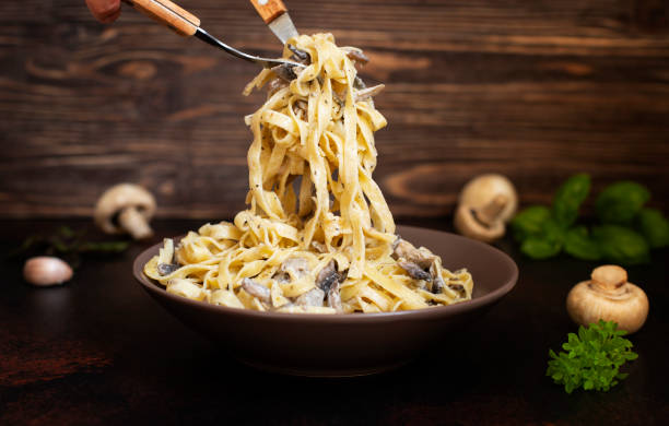 hausgemachte italienische fettuccine pasta mit pilzen und sahnesauce (fettuccine al funghi porcini). traditionelle italienische küche. serviert auf einem dunklen tisch mit einem rustikalen holzhintergrund. nahaufnahme - pasta stock-fotos und bilder