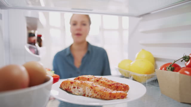 Young Woman Reaching Inside Refrigerator Of Healthy Food For Fresh Salmon On Plate