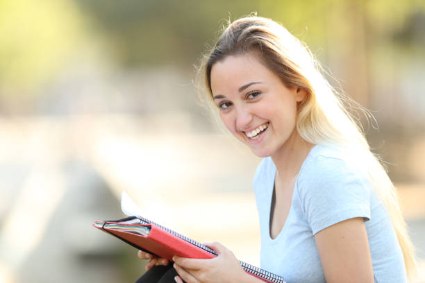 istock Happy student holding folder looking at camera in a park 1161200044