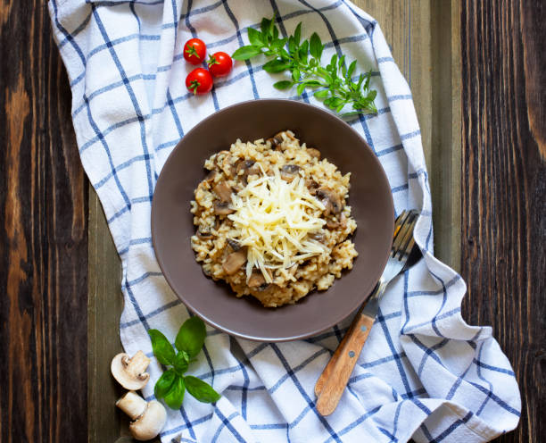 traditionelles italienisches gericht aus reis arborio risotto mit pilzen. serviert mit frischem basilikum, pilzen und kirschtomaten auf einem dunklen holztablett. ansicht von oben. - parmesan cheese risotto rice basil stock-fotos und bilder