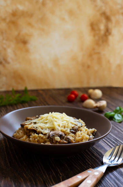 tradycyjne włoskie danie z ryżu arborio risotto z grzybami. podawane ze świeżą bazylią, grzybami i pomidorkami koktajlowymi na ciemnym drewnianym stole. pionowy. zbliżenie. jasne marmurowe tło - parmesan cheese risotto rice basil zdjęcia i obrazy z banku zdjęć