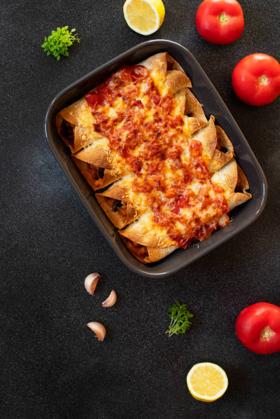 istock Mexican enchiladas with chicken, vegetables, corn, beans, tomato sauce and cheese. Served in baking tray. Mexican food. Latin American cuisine. Black background, top view, copy space 1161202764