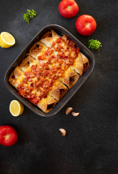 istock Mexican enchiladas with chicken, vegetables, corn, beans, tomato sauce and cheese. Served in baking tray. Mexican food. Latin American cuisine. Black background, top view, copy space 1161202868