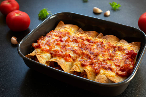 Mexican enchiladas with chicken, vegetables, corn, beans, tomato sauce and cheese. Served in baking tray. Mexican food. Latin American cuisine. Black background, close-up, copy space Mexican enchiladas with chicken, vegetables, corn, beans, tomato sauce and cheese. Served in baking tray. Mexican food. Latin American cuisine. Black background, close-up, copy space enchilada stock pictures, royalty-free photos & images