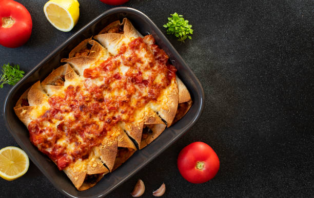 istock Mexican enchiladas with chicken, vegetables, corn, beans, tomato sauce and cheese. Served in baking tray. Mexican food. Latin American cuisine. Black background, top view, copy space 1161203087