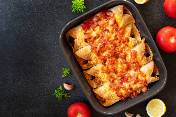 istock Mexican enchiladas with chicken, vegetables, corn, beans, tomato sauce and cheese. Served in baking tray. Mexican food. Latin American cuisine. Black background, top view, copy space 1161203184