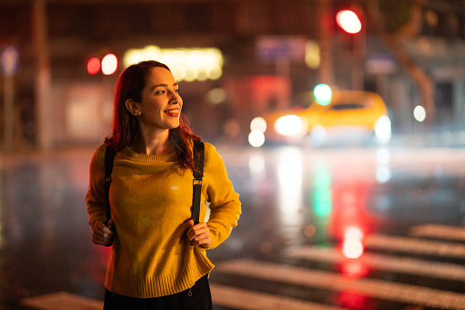 Young , smiling hipster woman walking on the street at night in Shanghai, holding backpack
