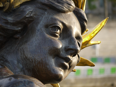 Paris, France - 05/17/2016 : Close-up of the head of one of the two nymphs of the Seine, bronze statue hanging on the deck of the Alexandre III bridge, which brandishes its golden scepter and shines in the light of the spring sun.