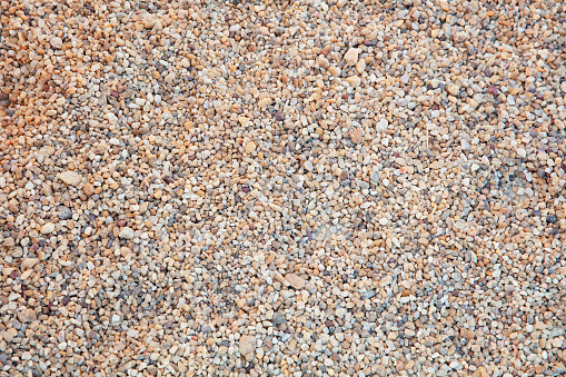 This image shows macro texture background of a worn concrete sidewalk, showing exposed aggregate stones from exposure to weather.