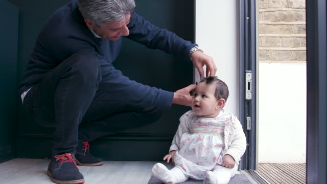 A father measures his baby daughter against a wall at home to see how tall she is