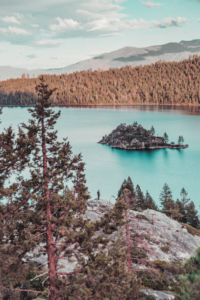 A hiker standing on boulders, enjoying the views of Fannette Island and Emerald Bay in the evening at Emerald Bay State Park, Lake Tahoe, California, USA.