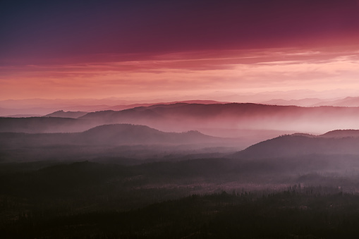 Rolling hills at Crater Lake National Park, Oregon, USA at sunrise. Pink/Orange sky, foggy layers of rolling hills.