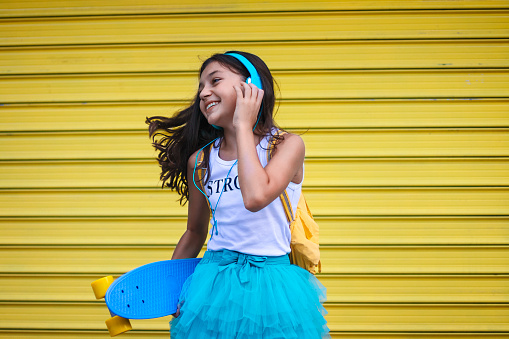 Beautiful teenage girl with headphones and skateboard listening music