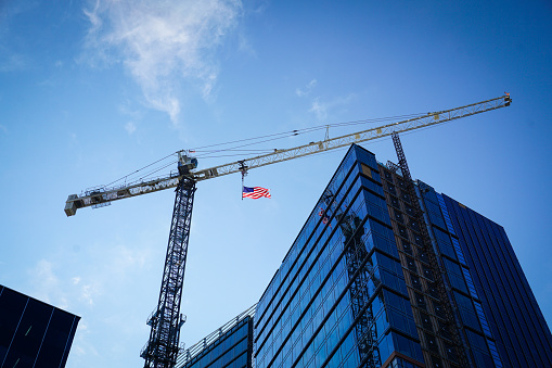 American flag flies from a large crane during the weekend of July 4th, reflecting in the mirrored windows of the building under construction