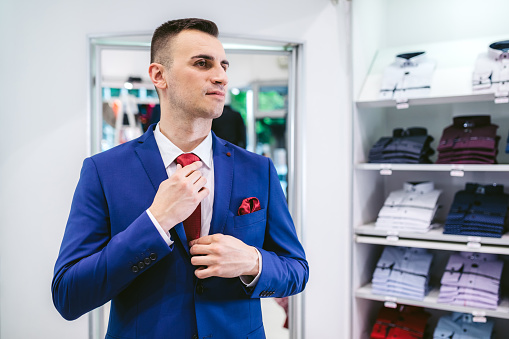 Young caucasian man buying suit in store.