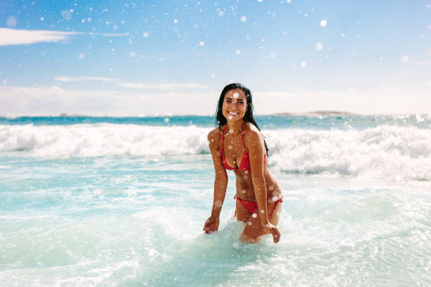 Woman on vacation playing at the beach Woman on vacation having fun at the beach playing in the water. Female in bikini enjoying splashing water at the beach. beach fashion stock pictures, royalty-free photos & images