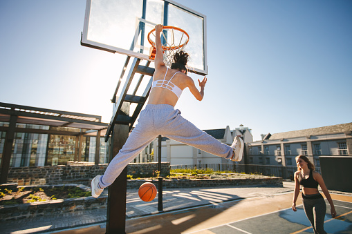 Females playing basketball on street court. Woman streetball player making slam dunk in a basketball game.