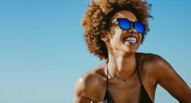 Cheerful woman on summer vacation Close up of cheerful african woman in sunglasses looking away and smiling. Young female in bikini having fun outdoors on summer vacation. beach fashion stock pictures, royalty-free photos & images