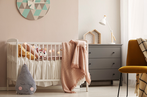 Pillows and toy in white wooden crib with pastel pink blanket in bright nursery