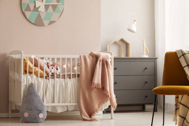 pillows and toy in white wooden crib with pastel pink blanket in bright nursery - equipamento de bebê imagens e fotografias de stock