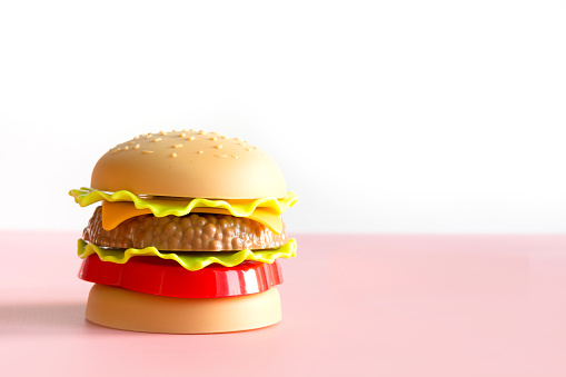 Plastic burger, salad, tomato with on pink background. Horizontal orientation. Childrens toy. Concept of harmful artificial food. Plastic. Not organic. Not useful.