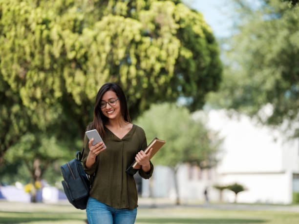 그녀의 스마트 폰을 확인하는 밀레니엄 대학생 - student printed media walking clothing 뉴스 사진 이미지