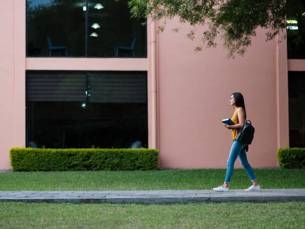 college girl walking through campus - adult education full length book imagens e fotografias de stock