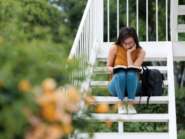 Concentrated university student sitting on steps reading Reading, Young Women,  Concentrated,Campus, Stairs, Student, Millennial, Latin, religious text stock pictures, royalty-free photos & images