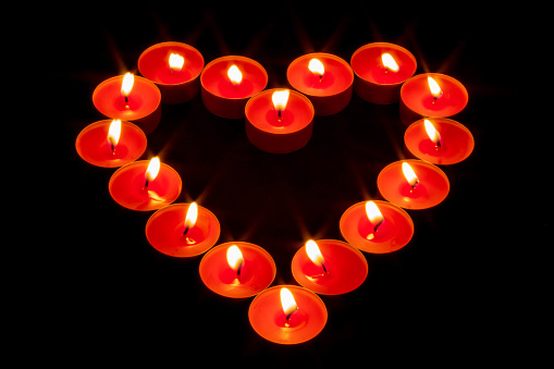 A heart made with red candles lit on a totally black background