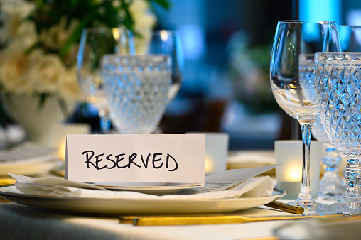 festive lunch outside at summer, table serving with white linen tablecloth, empty plate and bowl, wine glass, fork, spoon and silver knife, vase with flowers in green garden