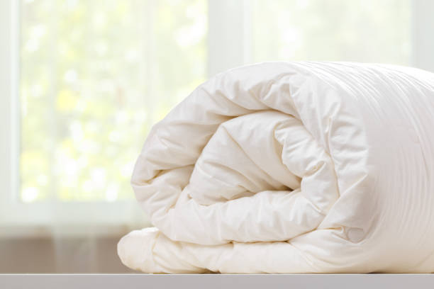 A folded rolls duvet is lying on the dresser against the background of a blurred window. Household. A folded rolls duvet is lying on the dresser against the background of a blurred window. Household. bedding stock pictures, royalty-free photos & images