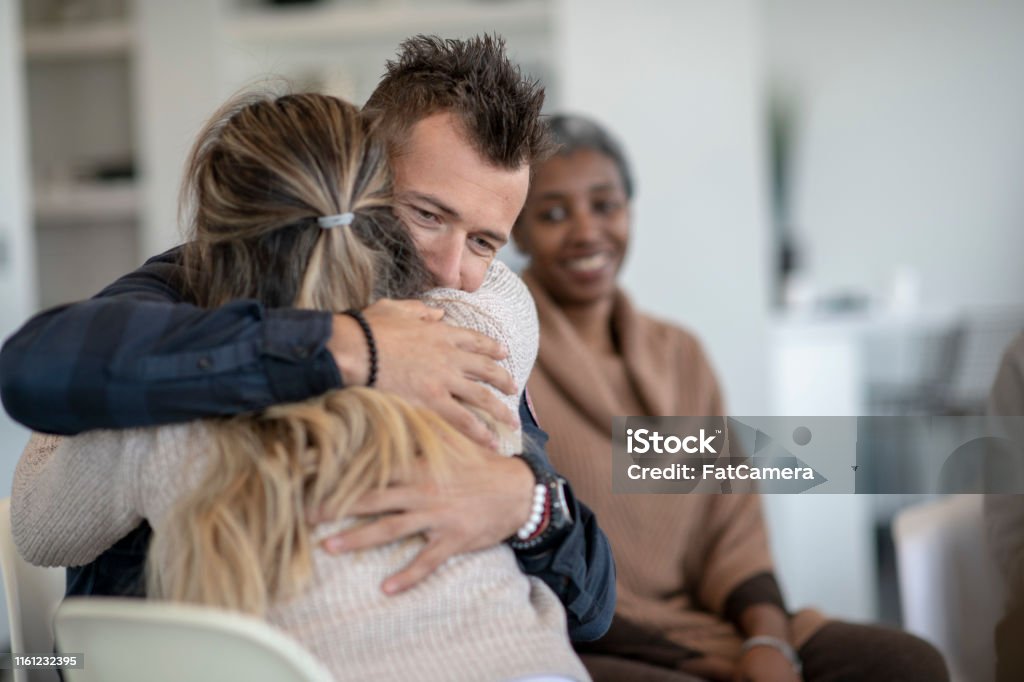 Showing support in group therapy A young caucasian man is hugging a female during a group therapy session. He is hugging her tight and feeling a sense of relief. Recovery Stock Photo