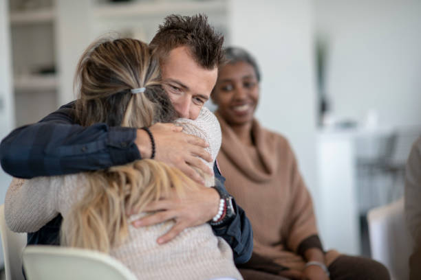 Showing support in group therapy A young caucasian man is hugging a female during a group therapy session. He is hugging her tight and feeling a sense of relief. alcohol abuse photos stock pictures, royalty-free photos & images
