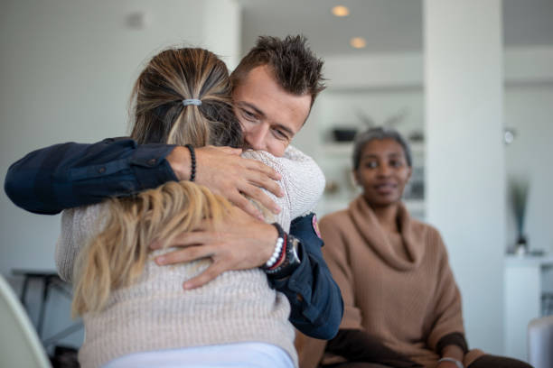 Showing support in group therapy A young caucasian male is hugging a female in a group therapy class. He is hugging her tight and feeling a sense of relief. alcoholics anonymous photos stock pictures, royalty-free photos & images