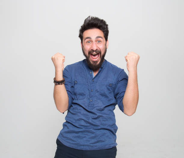 retrato de joven feliz animando sacudiendo el puño sobre el fondo gris - shaking fist fotografías e imágenes de stock