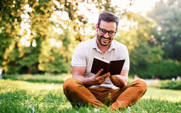 человек читает книгу в парке. образование, концепция образа жизни - men reading outdoors book стоковые фото и изображения